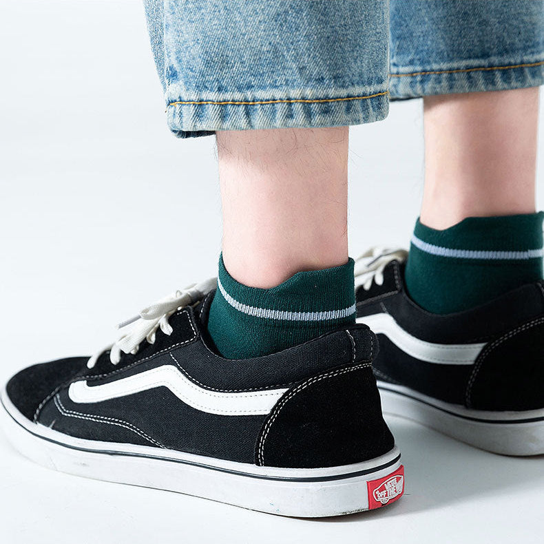Person wearing black sneakers with green socks on a white background