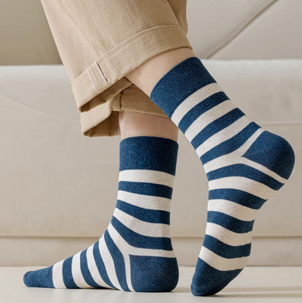 A person wearing navy blue and white striped crew socks with beige pants, shown from the knees down in a clean indoor setting.