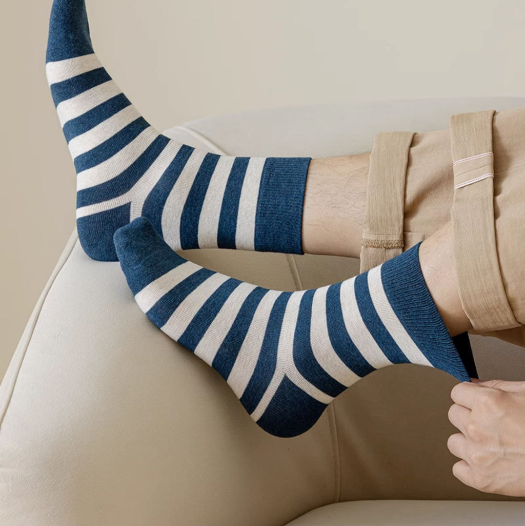 A person wearing navy blue and white striped ankle socks, shown with folded legs on a beige sofa. 