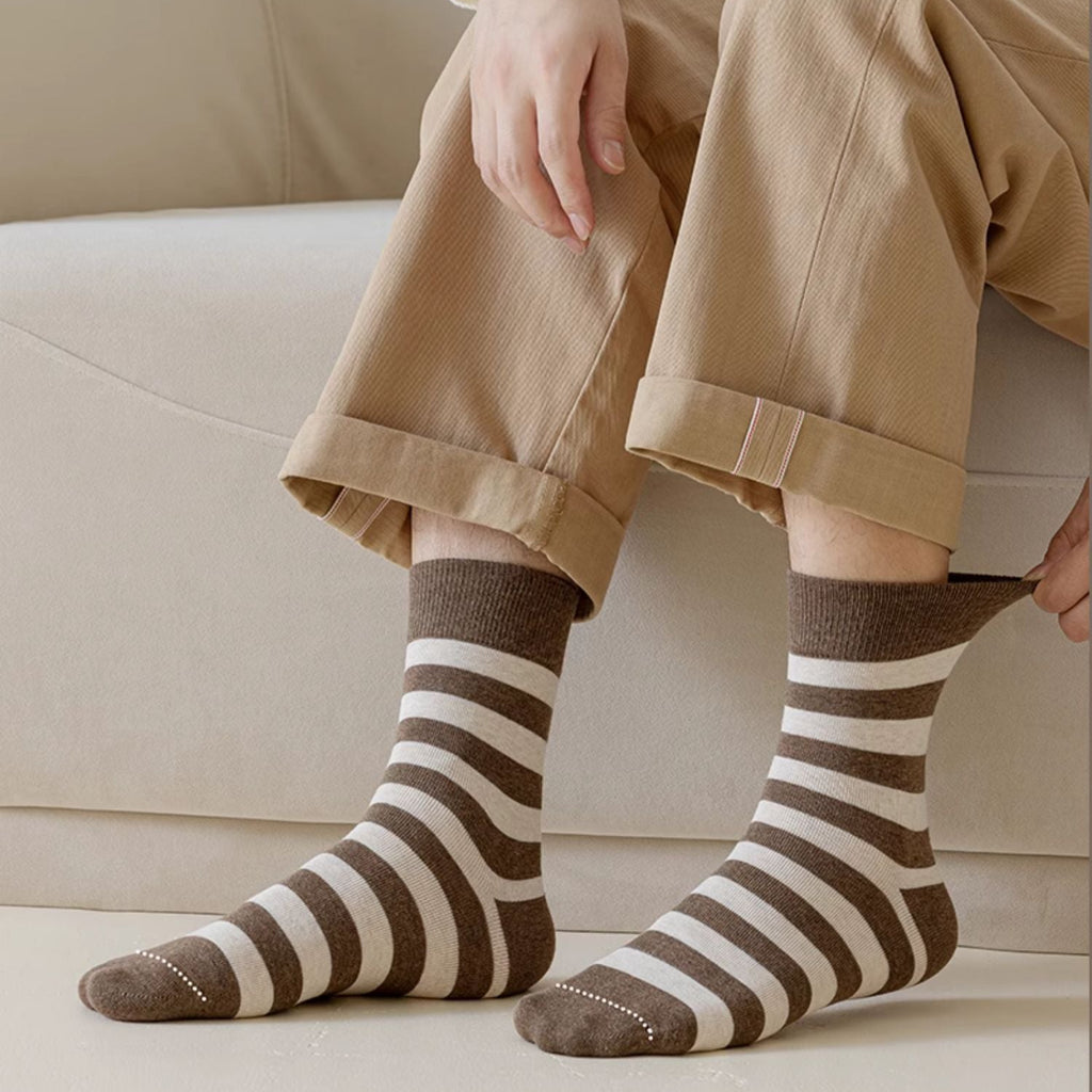 A person seated on a light beige sofa wearing brown and cream striped socks with cuffed tan pants and a white top. 