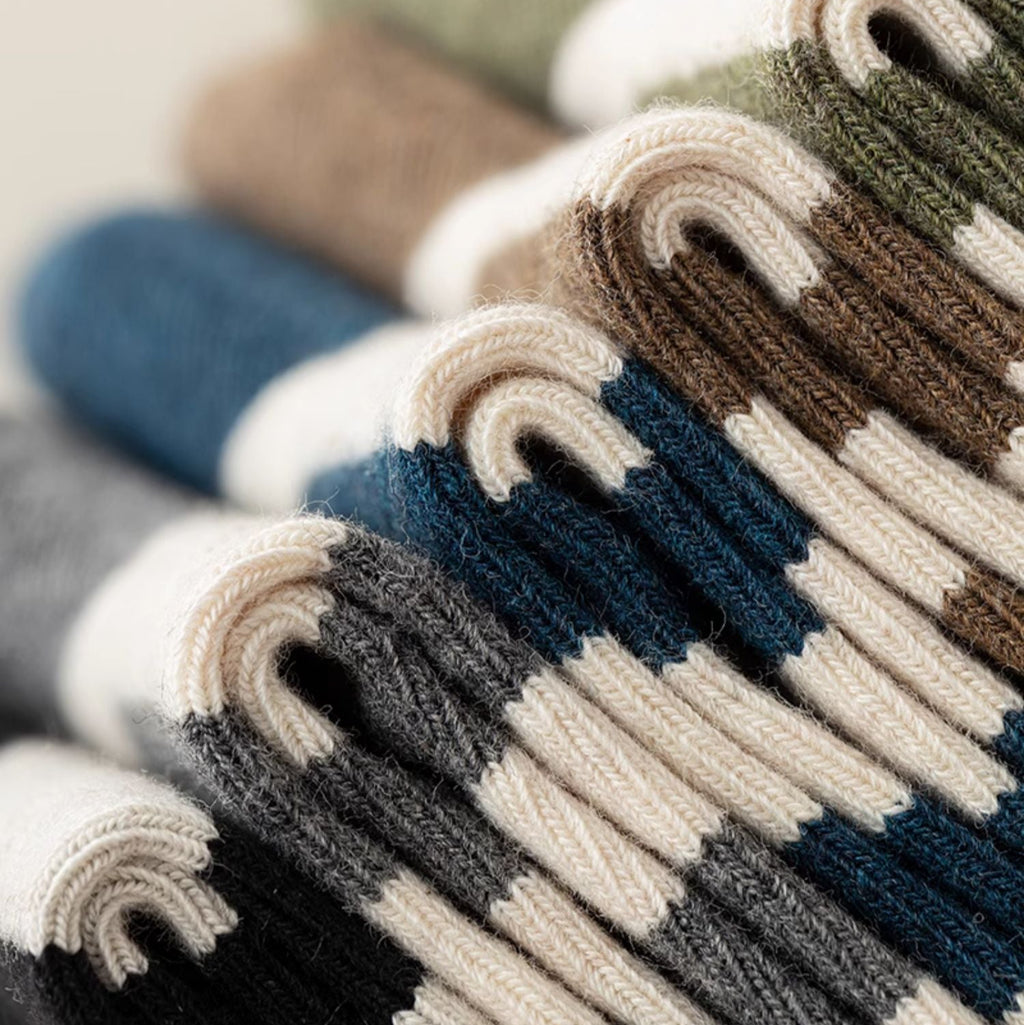 A close-up of folded striped knit socks or sweaters in multiple colors, including navy, blue, brown, beige, gray, and orange