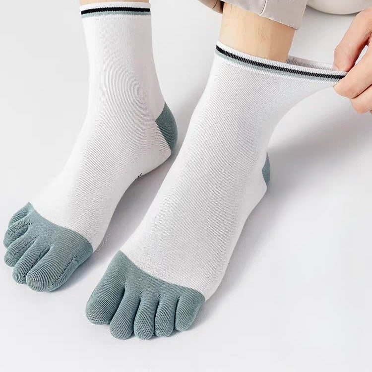 White five-toe socks with muted blue-gray toes and heels, shown on a person's feet with light beige pants. A hand is adjusting the cuff of the right sock.