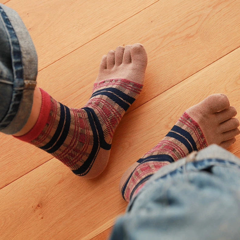 A close-up of a person's feet wearing patterned socks with red, navy, and beige stripes, standing on a light wood plank floor.