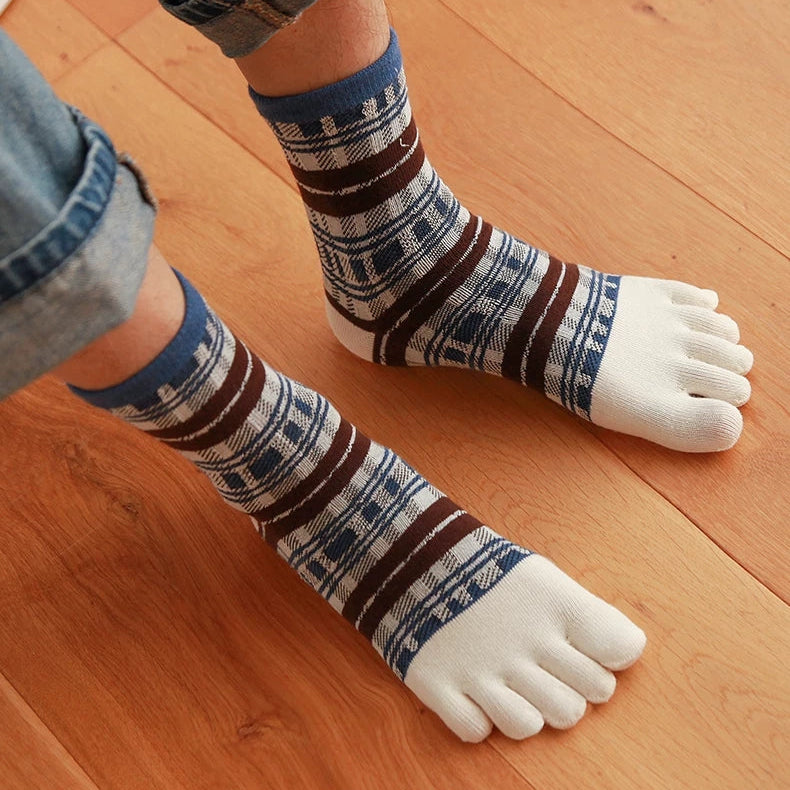A person wearing patterned toe socks with blue, brown, and white stripes, paired with rolled-up denim jeans, standing on a wooden floor.