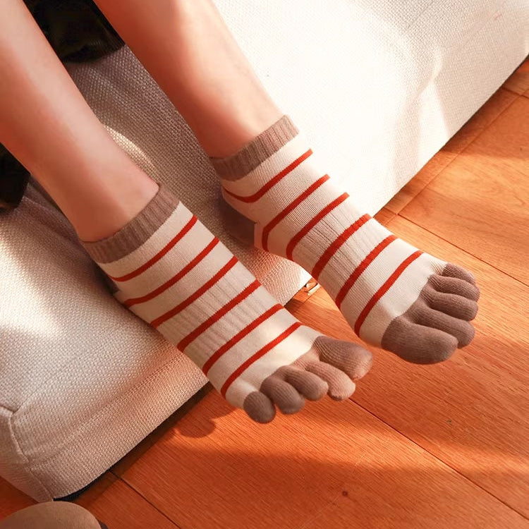 Person wearing striped socks with toes on a wooden floor