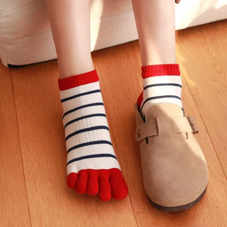 Person wearing red, white, and blue striped toe socks with beige clogs on a wooden floor.