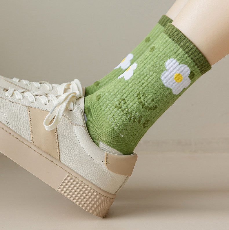 A person's leg wearing a light green ribbed crew sock with white daisy and smiley face patterns