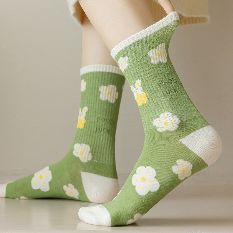 A person wearing light green crew socks with a white and yellow daisy pattern, paired with a cream-colored knit skirt. 