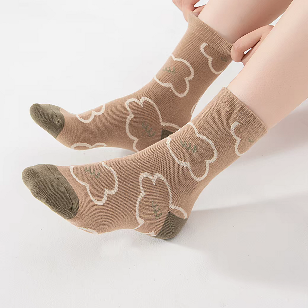 A pair of ankle socks worn on a person's feet, featuring a light brown base with cream-colored bunny outlines and darker brown toe and heel sections.
