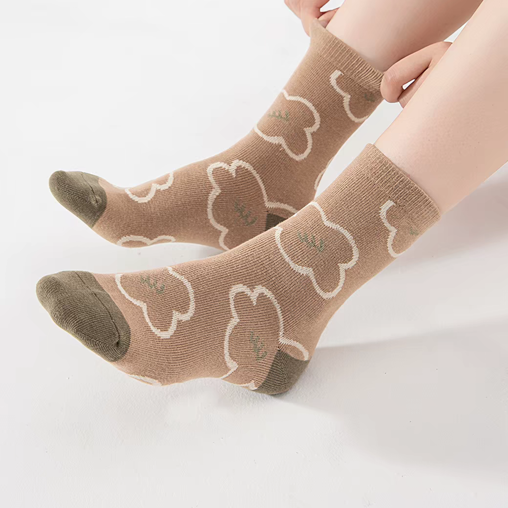 A pair of ankle socks worn on a person's feet, featuring a light brown base with cream-colored bunny outlines and darker brown toe and heel sections.