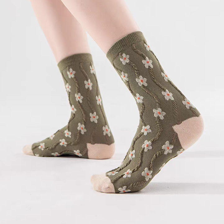 A pair of olive green crew socks with a floral pattern and beige heels, toes, and cuffs, shown on a model's feet against a white background.