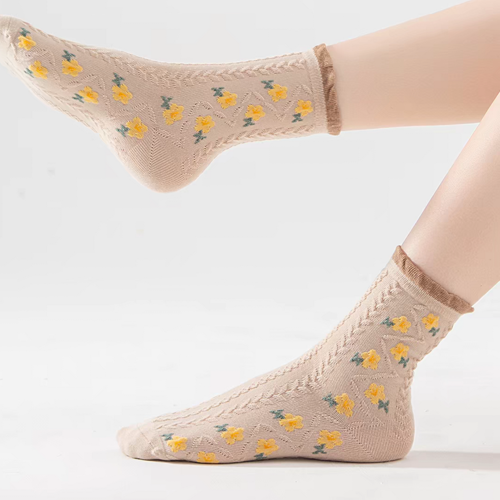 A pair of beige ankle socks with a yellow floral pattern and green leaf accents, shown on a model's feet against a clean white background.