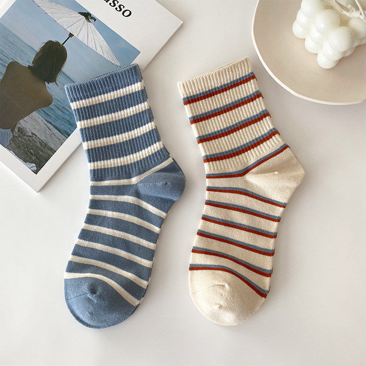 Two pairs of striped ankle socks displayed on a white surface. One sock is blue and white striped, and the other is cream with red and blue stripes.