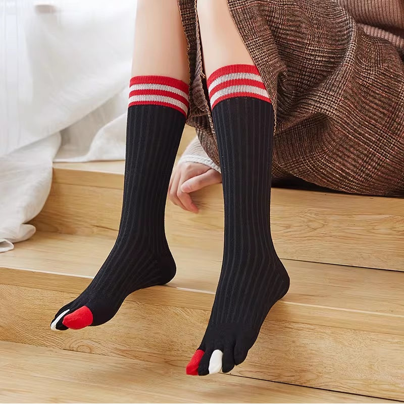 Person wearing black knee-high socks with red and white accents on a wooden floor.