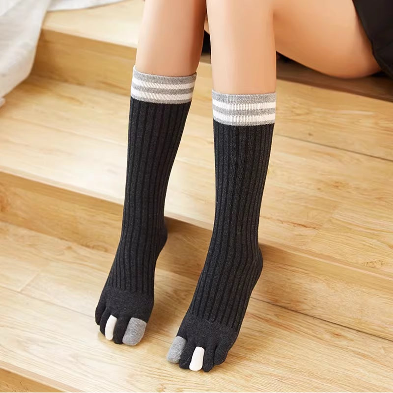 Person wearing black toe socks with gray accents on a wooden floor.