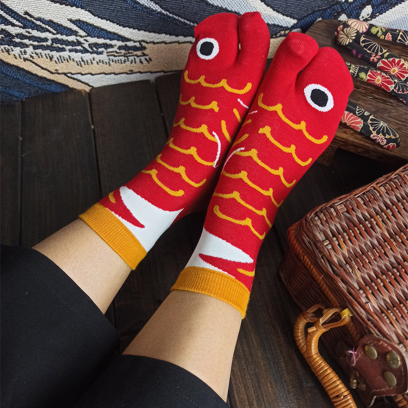Red and yellow fish-patterned socks worn with black pants on a wooden floor.